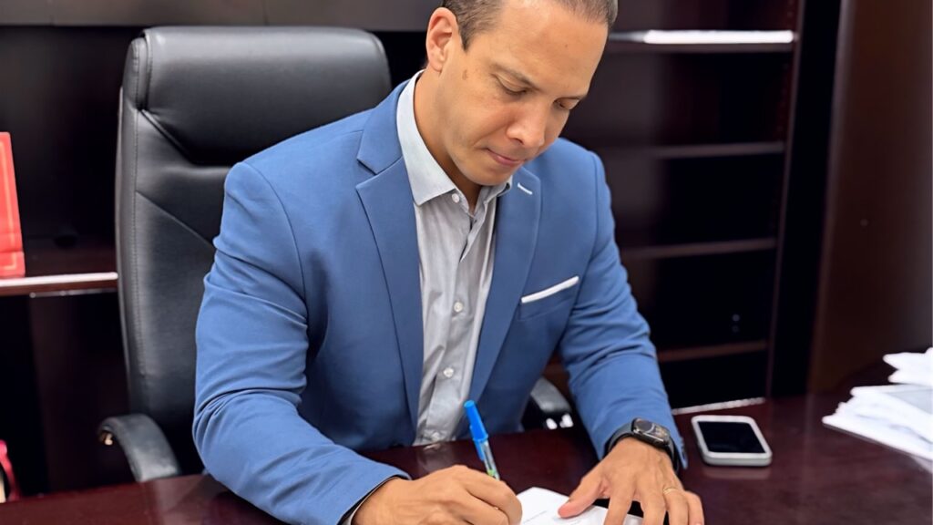 O prefeito de Limeira, Murilo Felix, assinando decreto, de paletó azul, camisa branca e caneta na mão